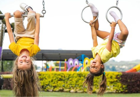 Twee meisjes hangen ondersteboven in een speeltuin